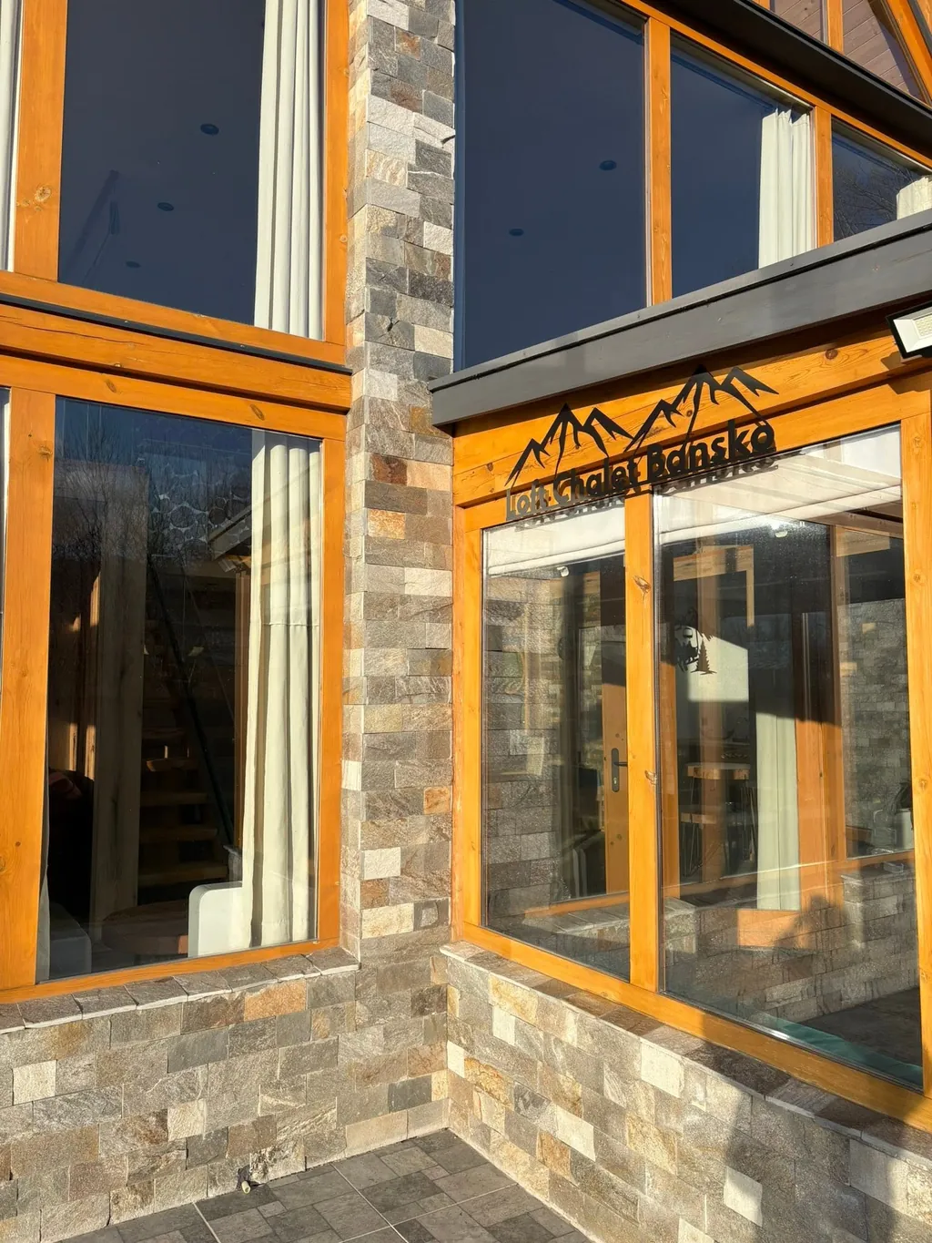 Входът на шалето с табелата „Loft Chalet Bansko“ над остъклената врата